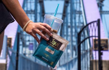 person holding cup and protein product with bridge in background